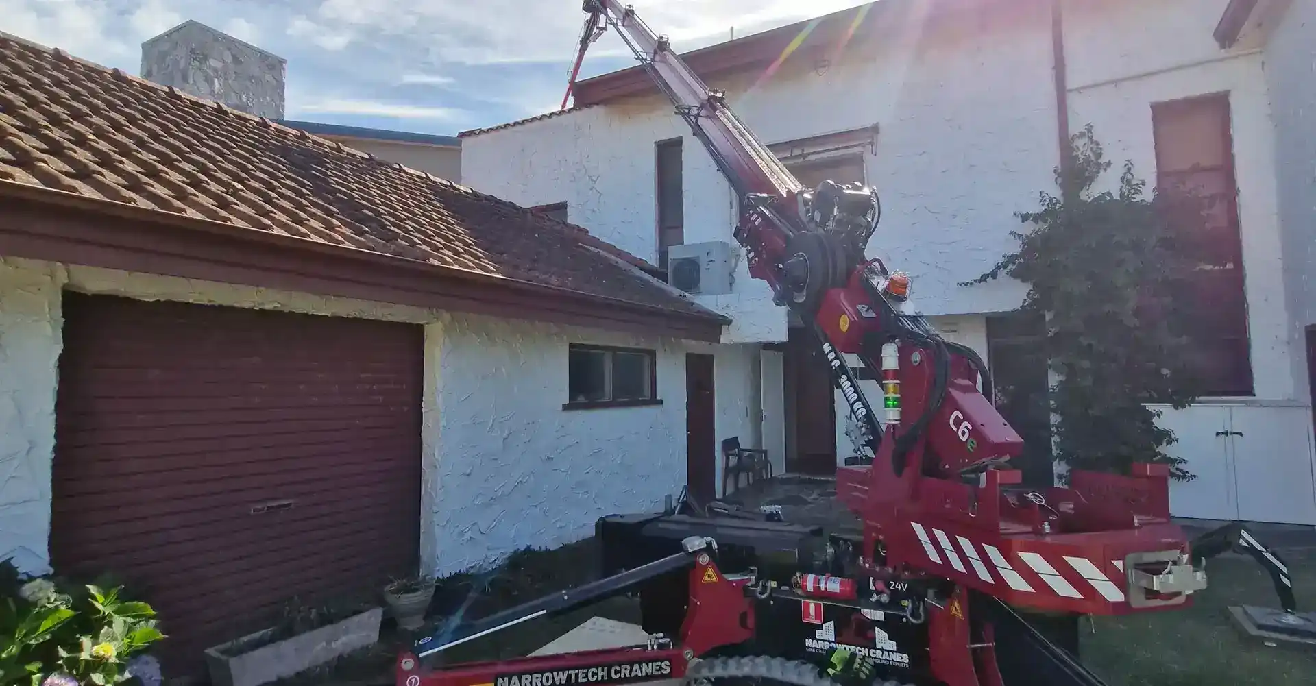 Narrowtech mini crane lifting materials over a fence line during a residential backyard renovation