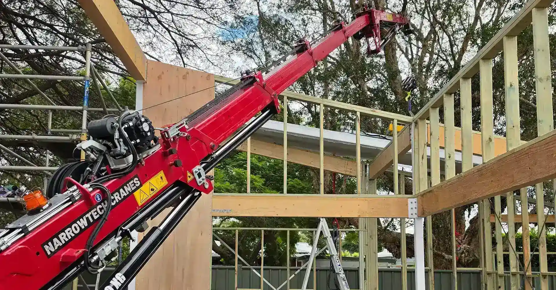 Narrowtech Cranes mini crane boom extended over a timber-framed house under construction